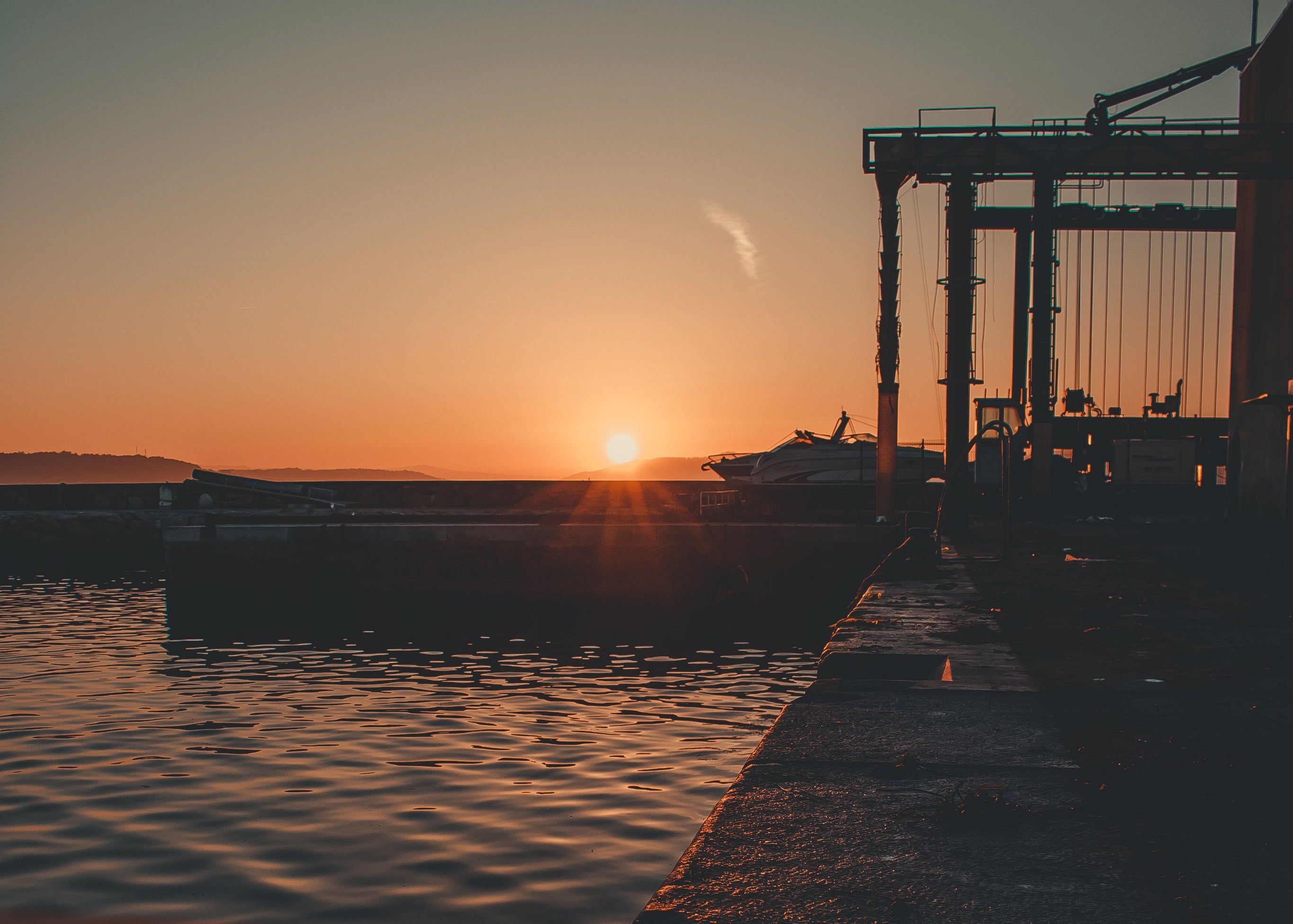 Sunset over a dock with boats and a crane, creating a warm glow.
